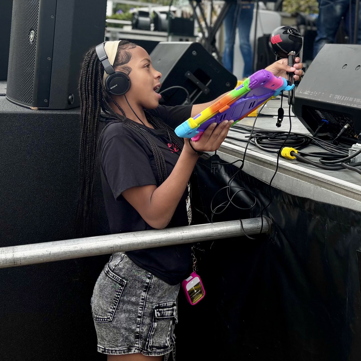 A young Be Loud Radio DJ singing into a colorful microphone on stage