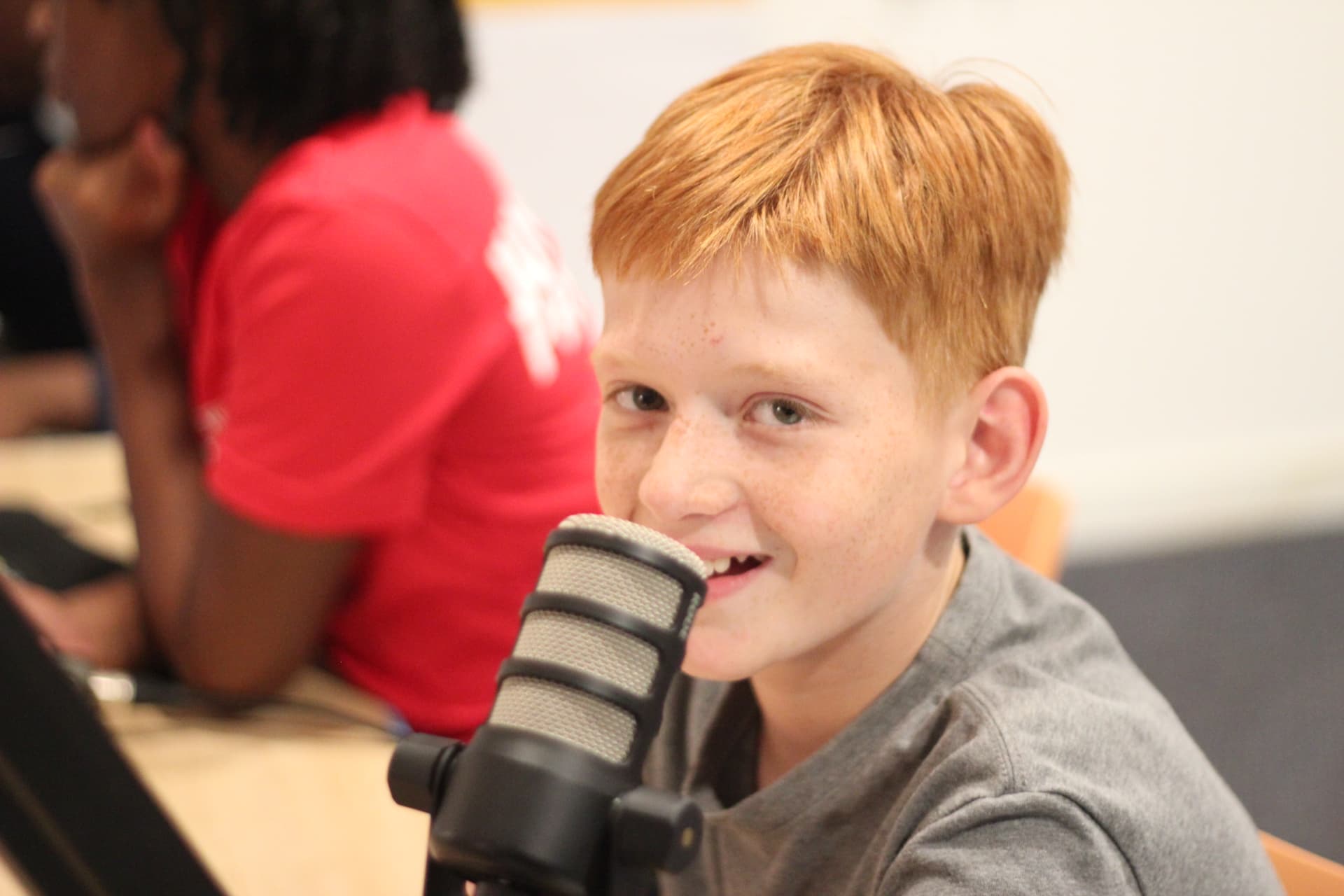 A young Be Loud Radio DJ smiling next to a studio microphone